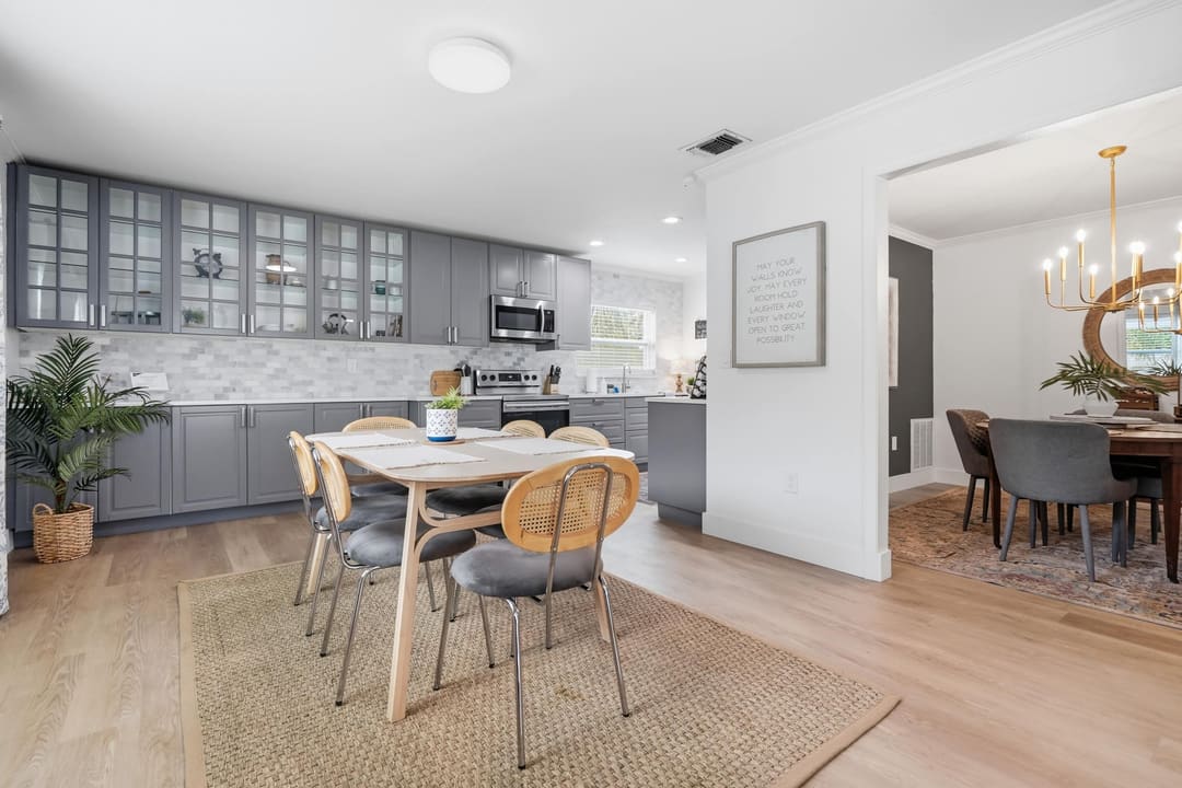 The kitchen with glass-front cabinets, cane breakfast chairs on a jute rug and the dining room beyond.