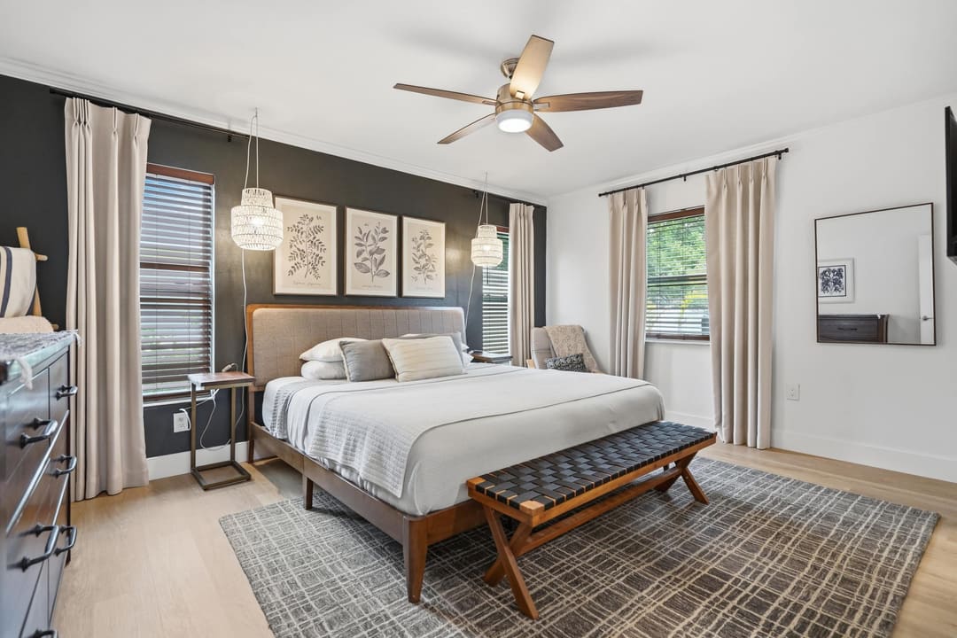 The primary bedroom, king bed against a deep green wall under twin rattan pendants.
