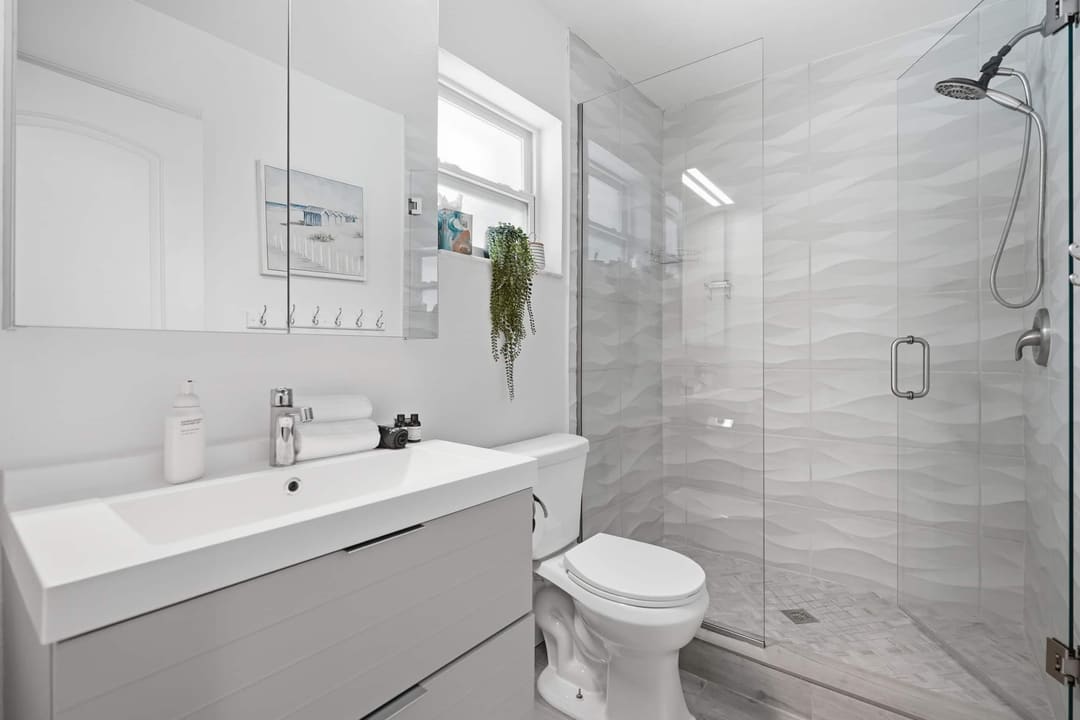 The en suite bathroom, glass walk in shower tiled in wave patterned stone, a trailing plant on the vanity.