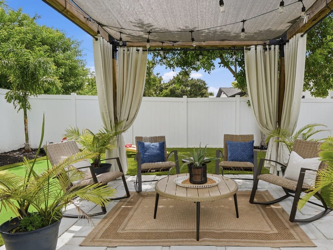 Under the pergola cabana: rockers around a table, potted palms and string lights overhead.