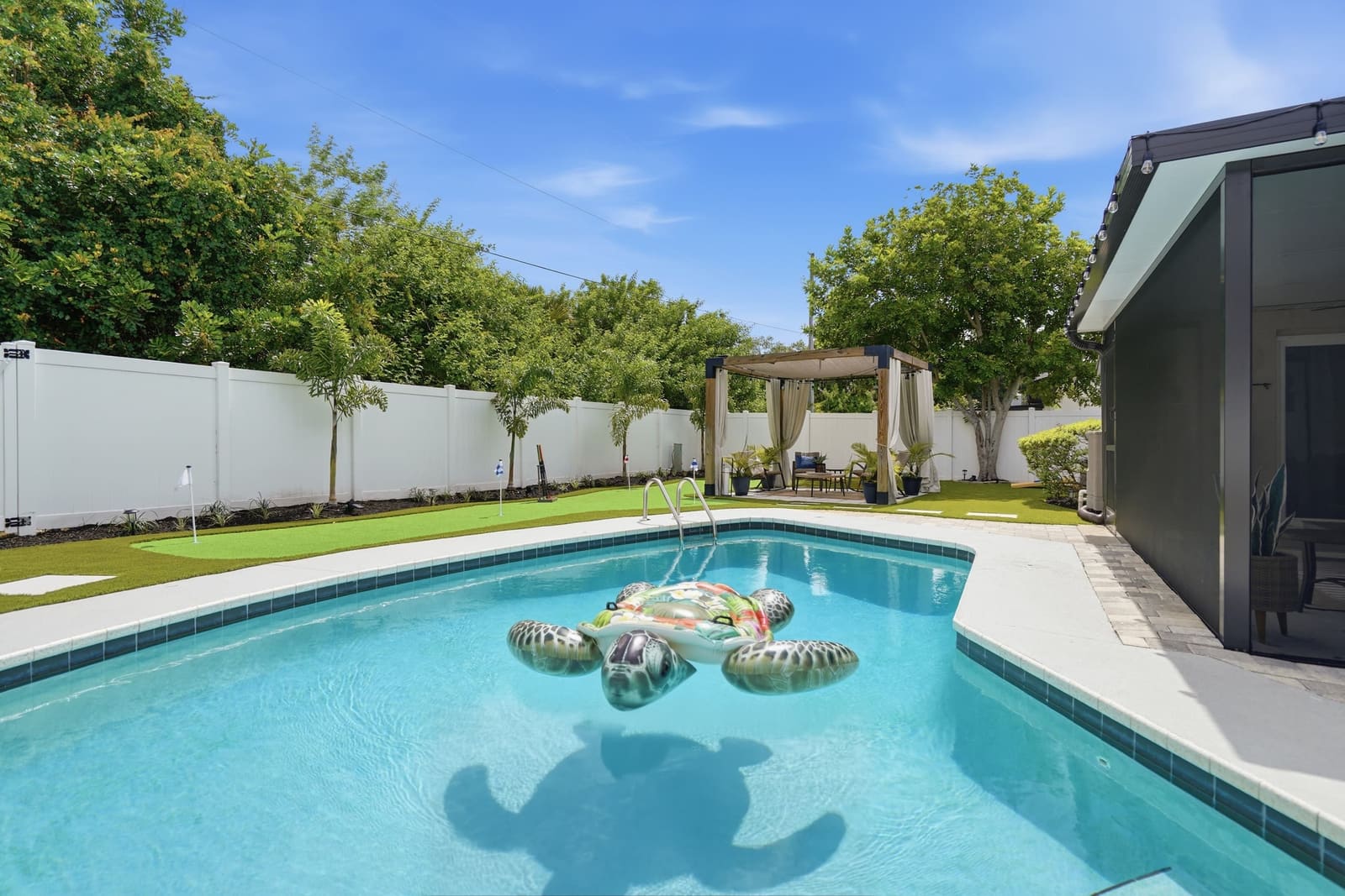 The pool at water level, the putting green and cabana along the fence beyond it, at a Dunedin, Florida vacation rental.