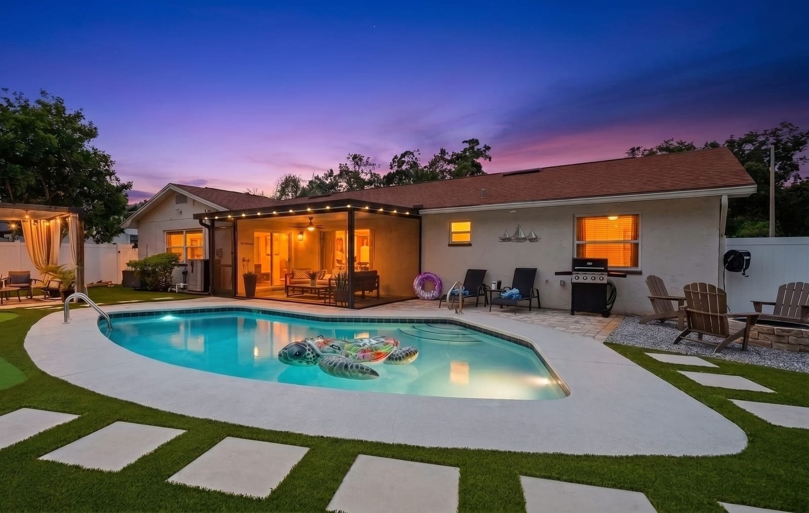 The pool lit from inside at dusk, string lights along the screened lanai and the cabana glowing at the far end of the yard.